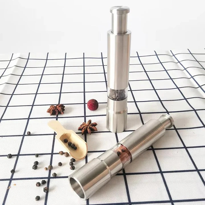 Two silver pepper mills on a checkered tablecloth with peppercorns and star anise.