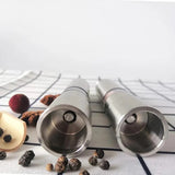 Two silver salt and pepper shakers on a white surface with black lines.