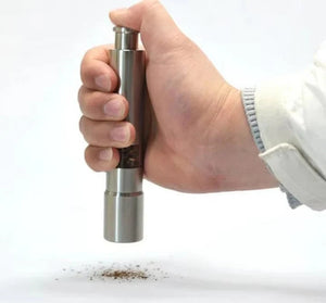 Hand holding a pepper grinder with ground pepper on a white background